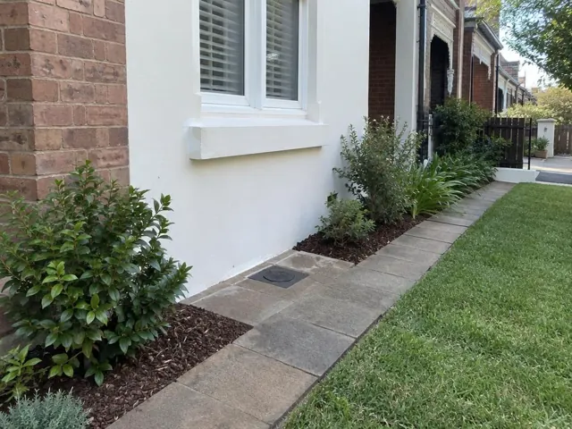 Flush capped access point in a paved garden path beside a brick and rendered house in Annandale